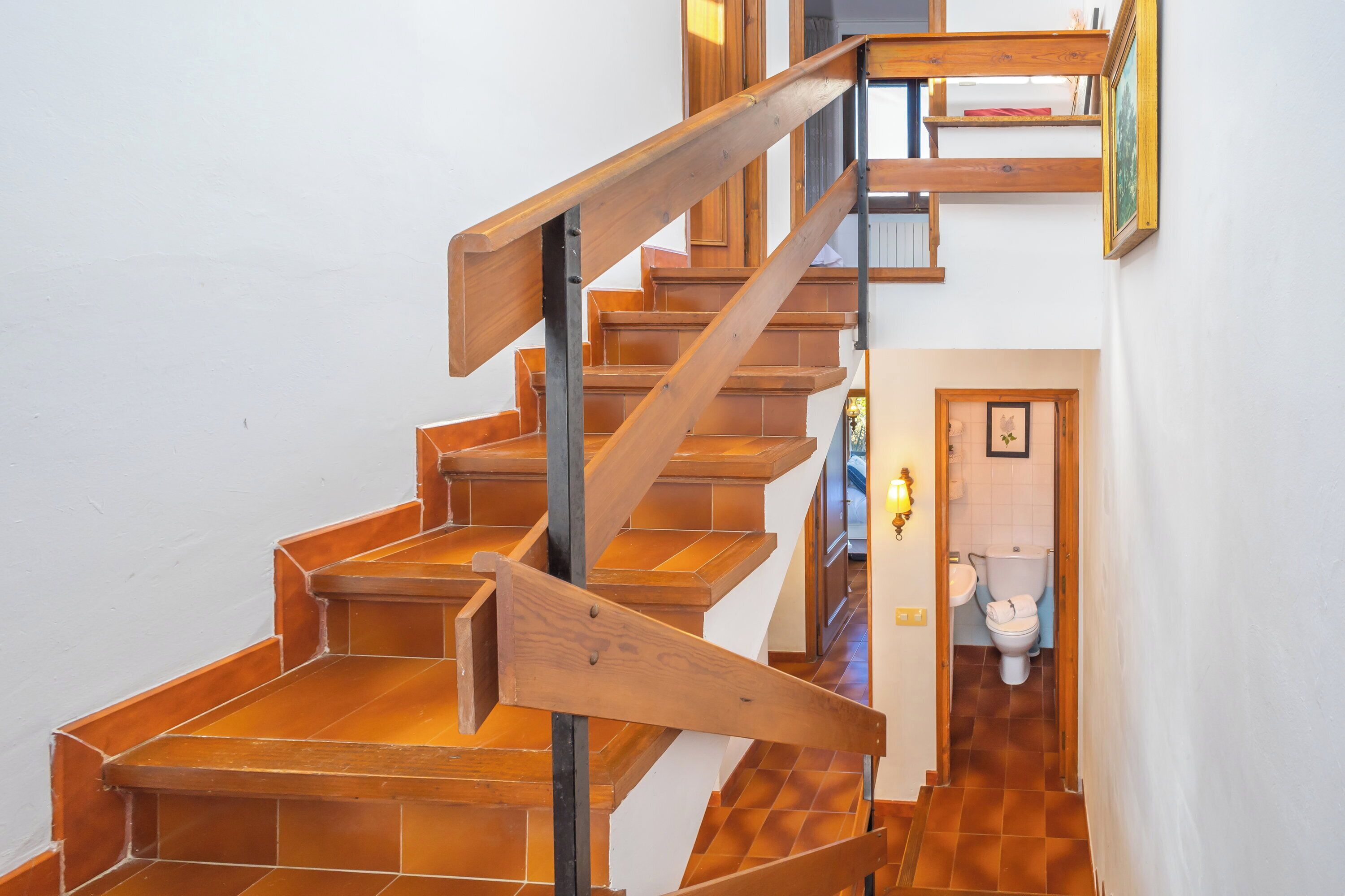A wooden staircase with a metal handrail leading to a bathroom with a toilet and sink.