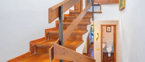 A wooden staircase with a metal handrail leading to a bathroom with a toilet and sink.