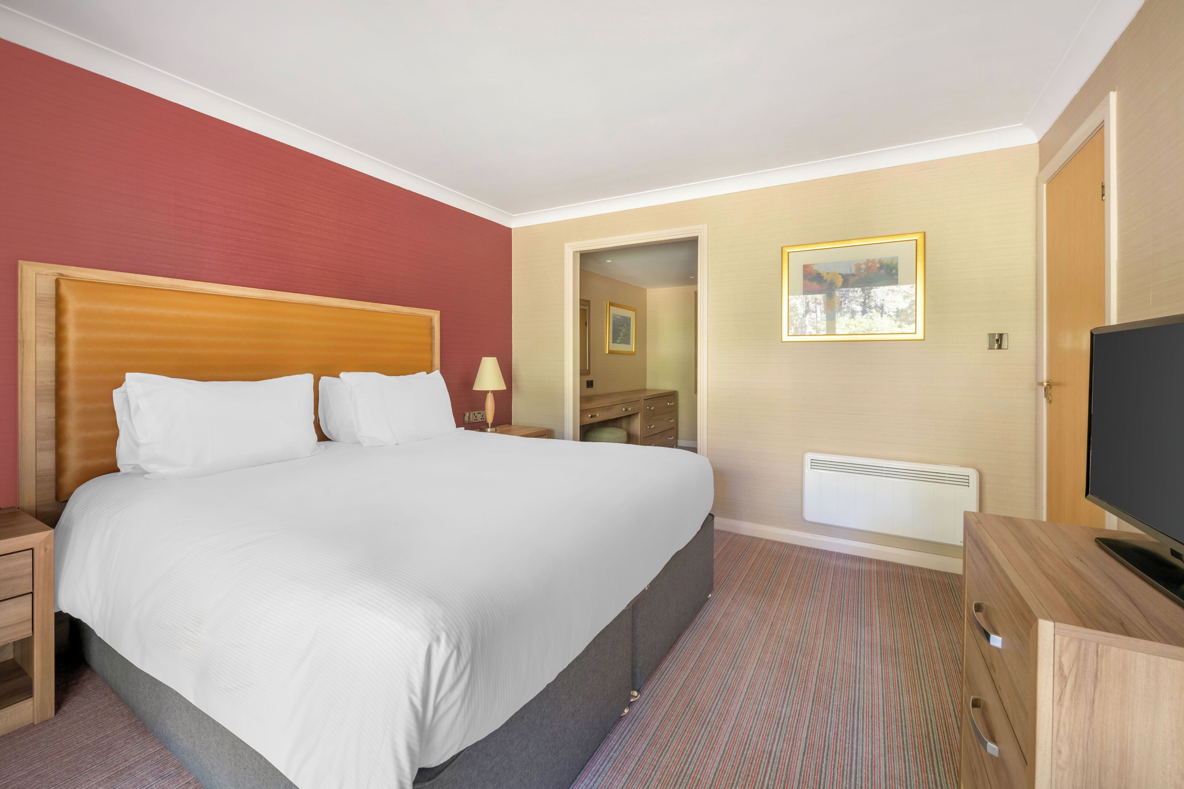 A hotel room with a large bed, a television, a dresser, and a mirror.