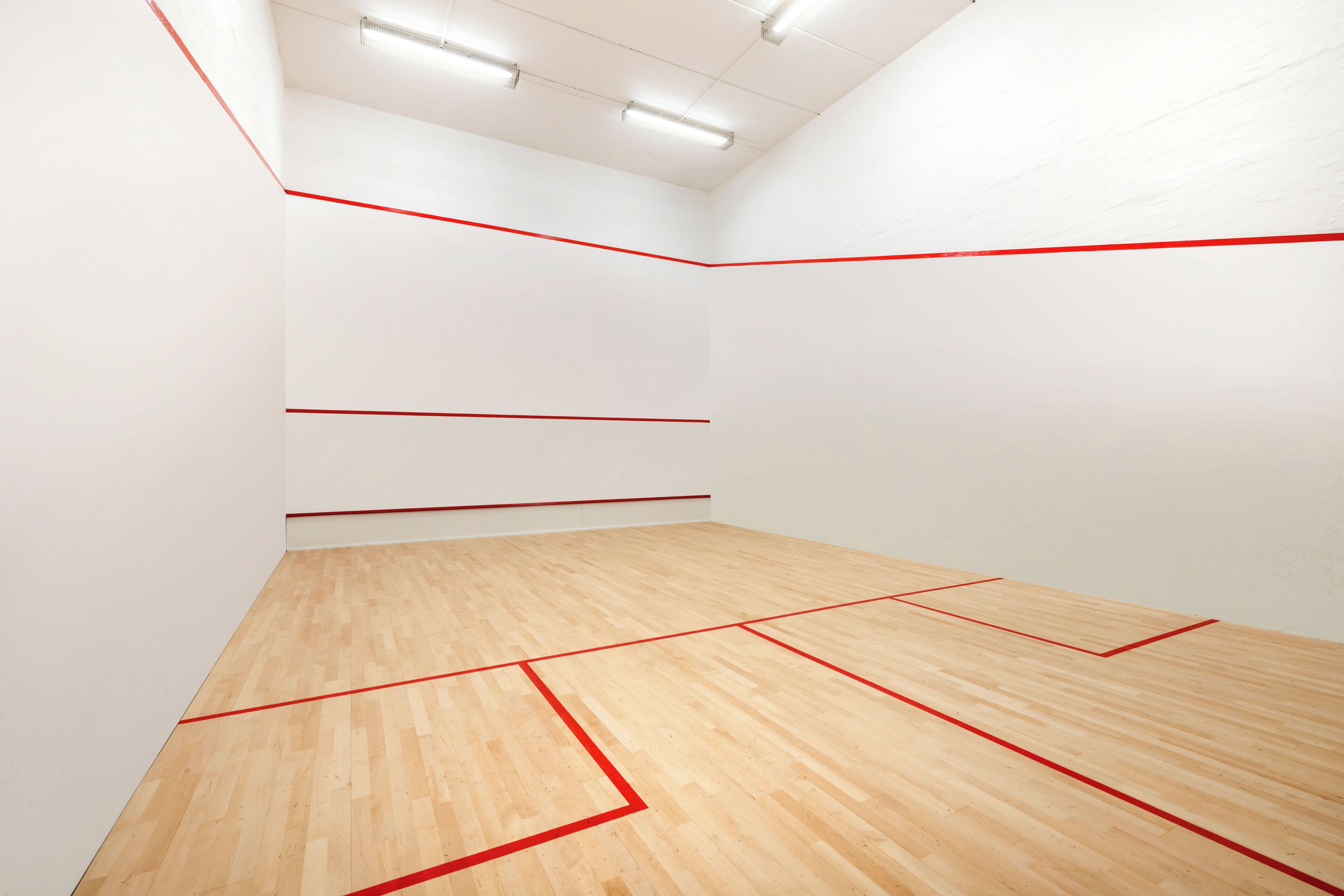 A squash court with wooden flooring and red boundary lines.