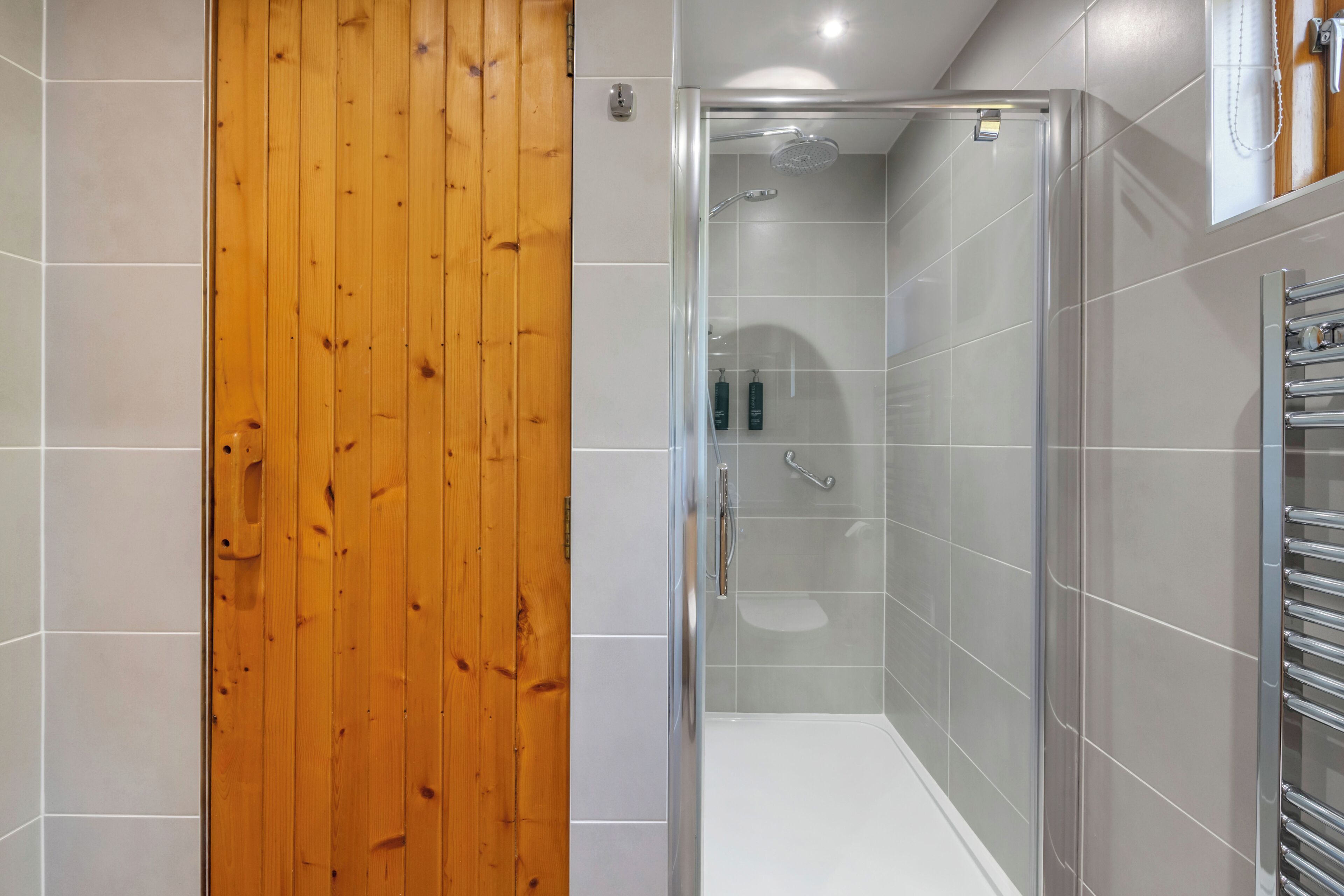 A modern bathroom with a glass shower enclosure, a wooden door, and a towel rack.