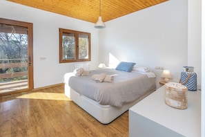 Ein Schlafzimmer mit einem Bett, Nachttischlampen, einem Fenster und Blick ins Freie.