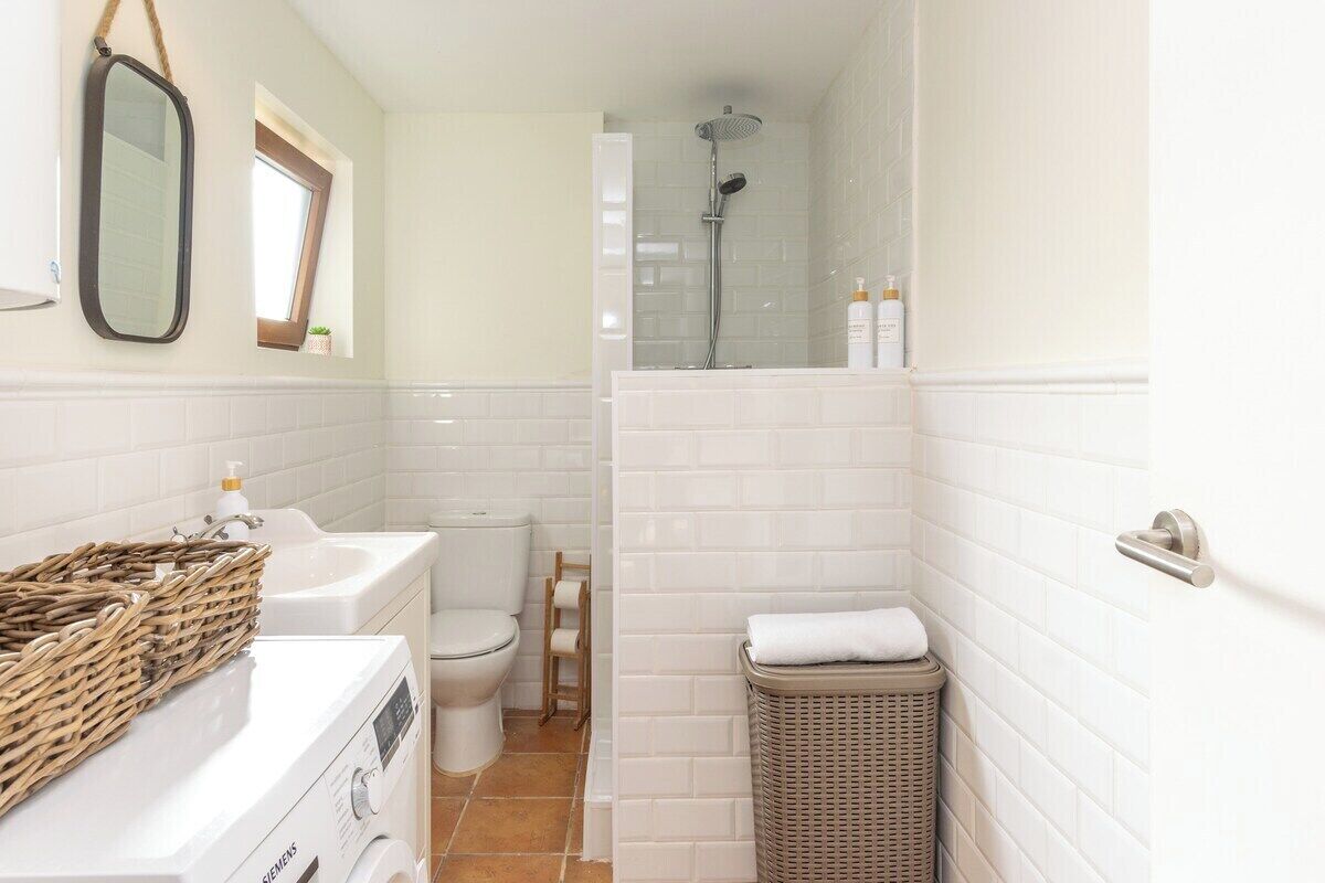 A bathroom with a washing machine, a toilet, a shower, and a wicker basket.