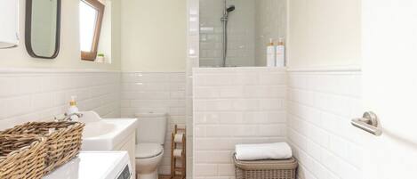 A bathroom with a washing machine, a toilet, a shower, and a wicker basket.