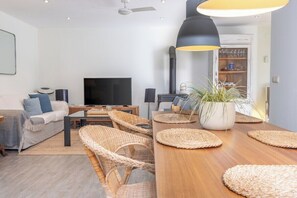 Ein modernes Wohnzimmer mit einer Couch, einem Fernseher, einem Esstisch und Korbstühlen.