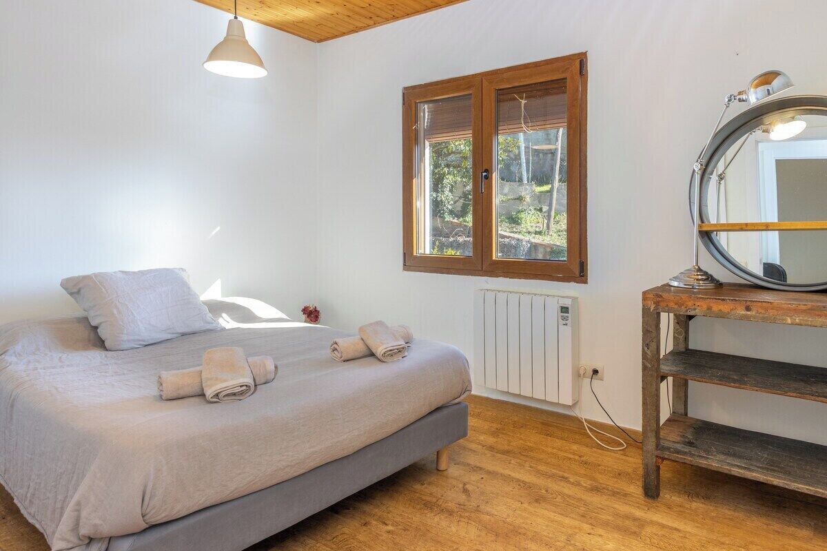 A bedroom with a bed, a window, a radiator, and a mirror on a wooden table.