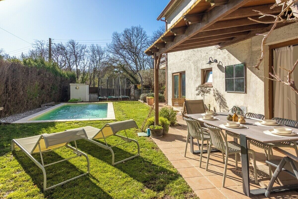 Un patio trasero con piscina, mesa y sillas en el patio, y un pequeño edificio con ventana.