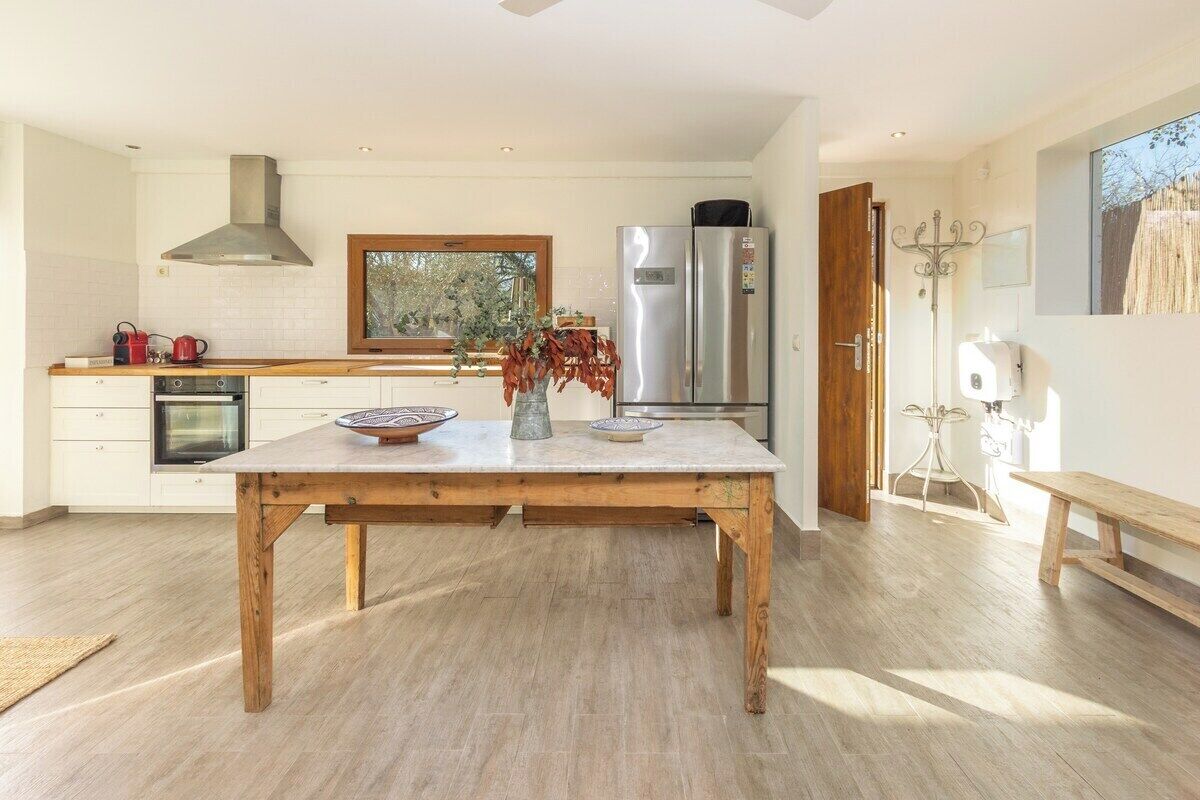 A modern kitchen with a wooden table, stainless steel appliances, and a window overlooking greenery.