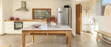 A modern kitchen with a wooden table, stainless steel appliances, and a window overlooking greenery.
