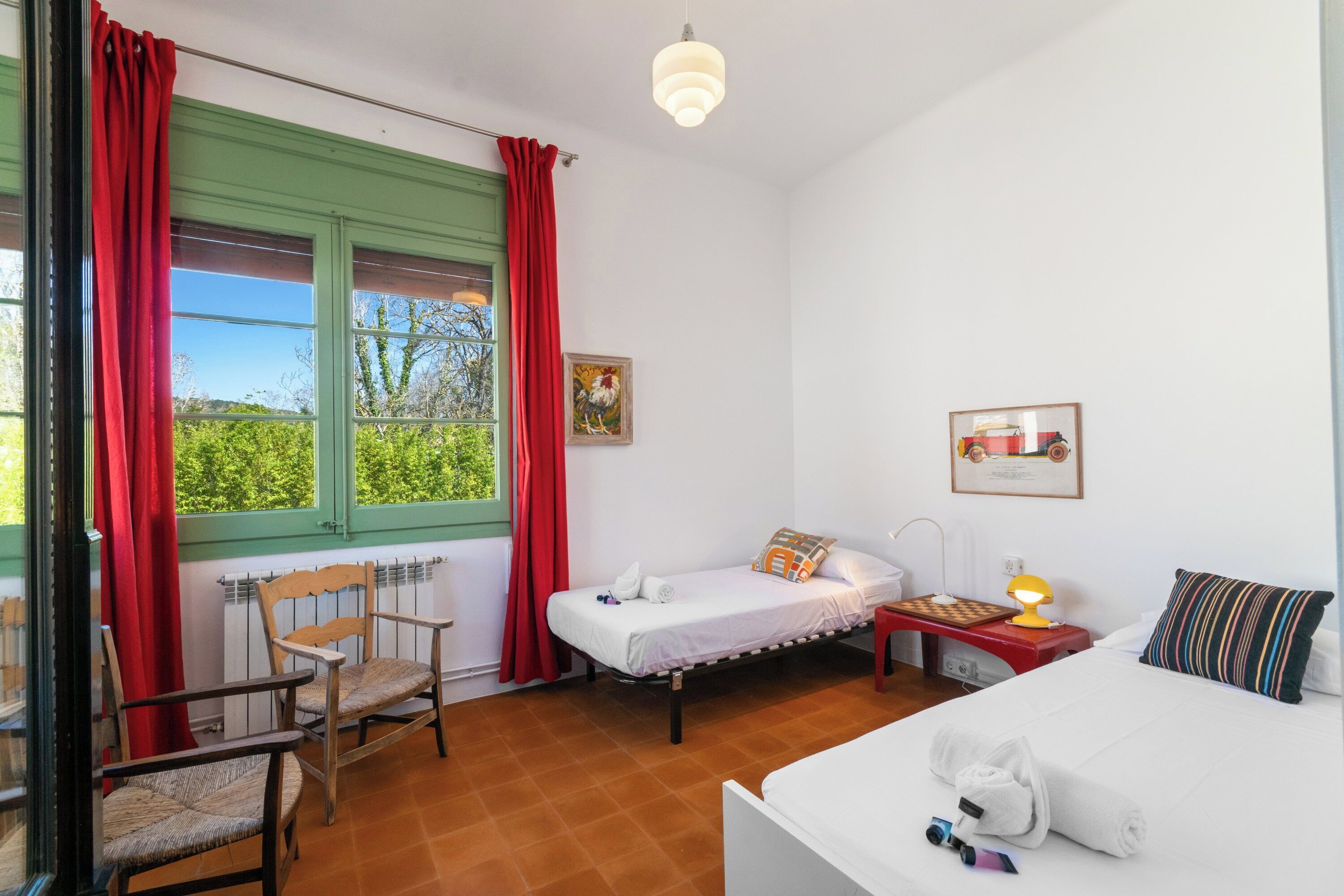 A room with a bed, a chair, a small table with a lamp, and a window with curtains.