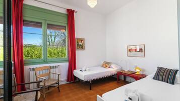 A room with a bed, a chair, a small table with a lamp, and a window with curtains.