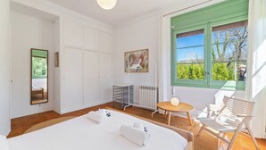 Et hotelværelse med en seng, et lille bord, en stol, en radiator, et vindue med udsigt og et billede på væggen.