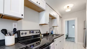A modern kitchen with white cabinets, a black stove, and a stainless steel sink. - Walk to VCU & Allianz Amphitheater  Cozy & Clean (Richmond)