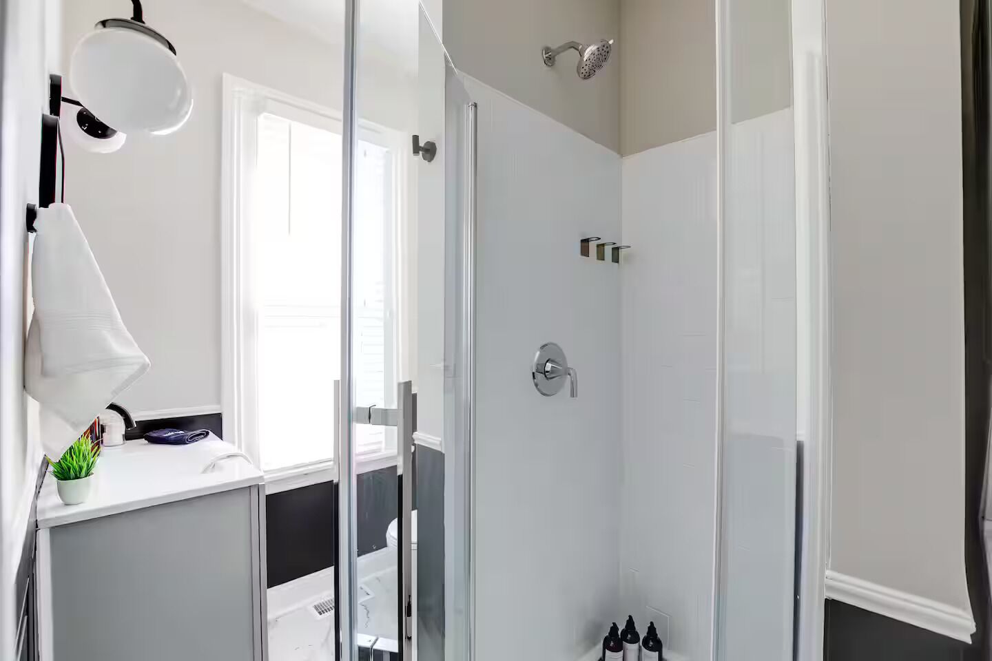 Et moderne badeværelse med brusekabine i glas, et hvidt toiletbord med spejl og en lille potteplante.