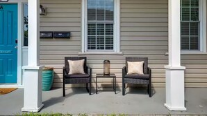 A porch with two wicker chairs, a small table, and a blue door. - Walk to VCU & Allianz Amphitheater  Cozy & Clean (Richmond)