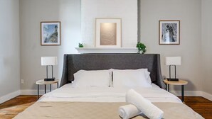 A hotel room with a large bed, two bedside tables with lamps, a fireplace, and framed artwork on the walls. - Walk to VCU & Allianz Amphitheater  Cozy & Clean (Richmond)
