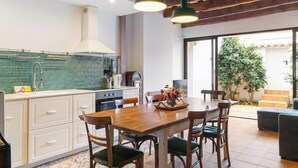 A modern kitchen with white cabinets, a wooden dining table, and hanging green pendant lights. - Casa con patio, piedra y luz natural (Sant Pere de Ribes)