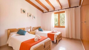 A room with two beds, wooden beams on the ceiling, a window with curtains, and a door. - Villa Roqueta (Pollença)