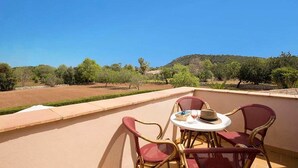 A balcony with wicker chairs and a table, overlooking a landscape with trees and a hill. - Villa Roqueta (Pollença)