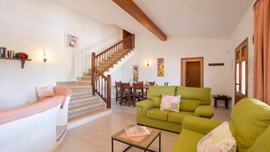 A living room with a staircase, a dining area, and a green sofa. - Villa Roqueta (Pollença)