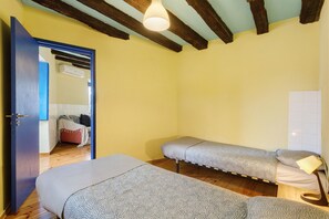 Ein Zimmer mit zwei Einzelbetten, Holzboden, Deckenbalken und einer Tür zu einem weiteren Raum.
