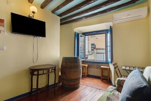 A room with a television mounted on the wall, a wooden barrel, a small table, and a window with a view of buildings outside. - Apartment 'Way To Castle - Alfama 6' with Wi-Fi and Air Conditioning (Lisboa)