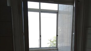 Ein Zimmer mit Fliesenboden, einem blauen Sofa, einem kleinen Tisch mit Tablett und einem Fenster mit Blick auf Bäume.
