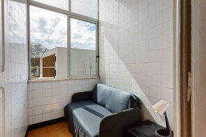 Ein Eckzimmer mit Fenster, einer Couch, einem kleinen Tisch und einer Lampe.