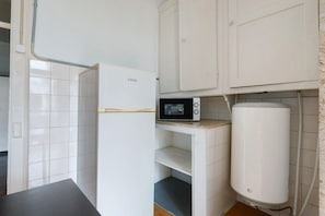 Eine Küche mit weißen Schränken, einem Kühlschrank, einer Mikrowelle und einem Durchlauferhitzer.