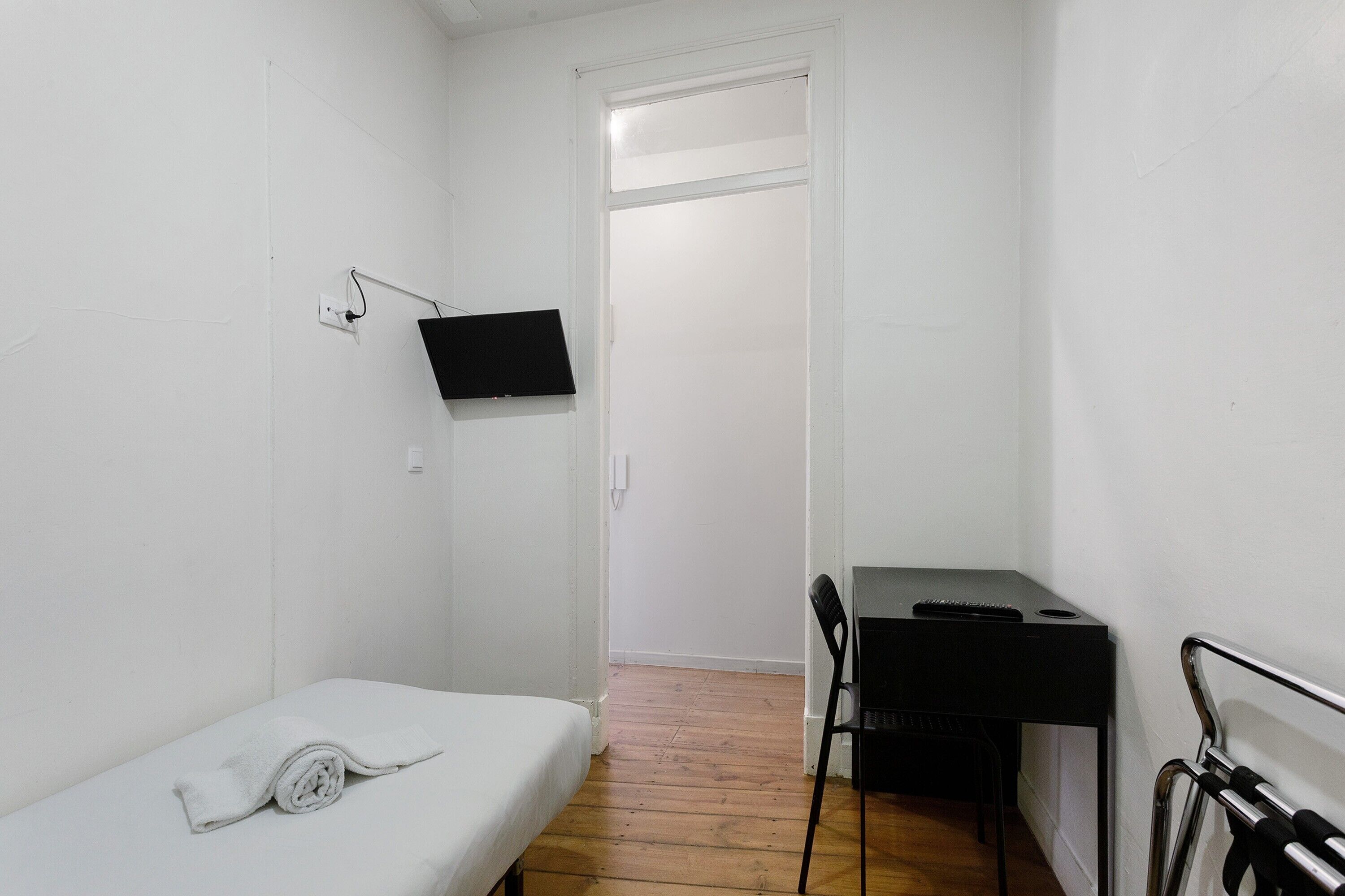 Una habitación pequeña y blanca con una cama, un escritorio y una silla.