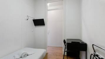 Una habitación pequeña y blanca con una cama, un escritorio y una silla.