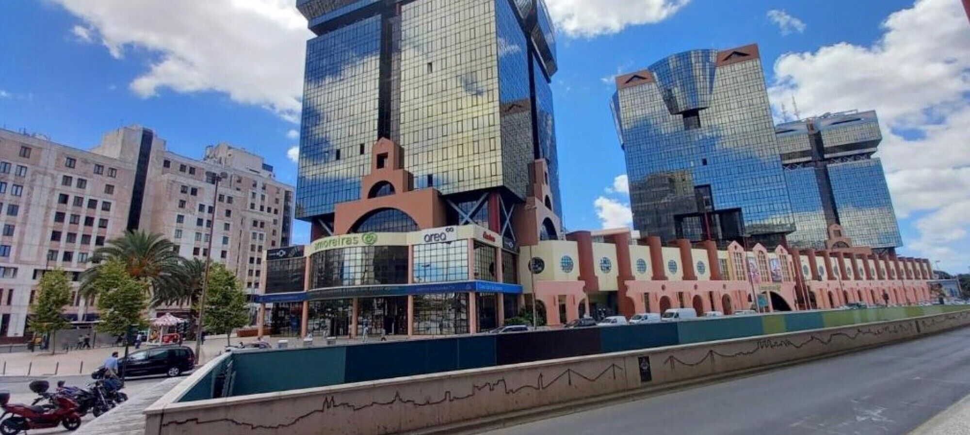 A modern building with a glass facade, a central atrium, and a series of smaller structures attached to its base.