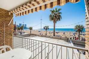 Uma varanda com vista para uma praia, palmeiras e céu limpo.