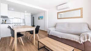 Eine moderne Küche mit weißen Schränken, einem Esstisch mit Stühlen, einer Couch mit Decke und einem Spiegel an der Wand.