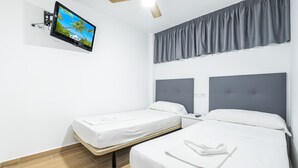 Ein Hotelzimmer mit zwei Einzelbetten, einem an der Wand befestigten Fernseher und einem Fenster mit grauem Vorhang.