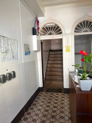 Ein Flur mit Fliesenboden, einer Treppe und einem an der Wand befestigten Handdesinfenspender.