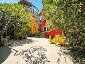 A courtyard with a yellow bench, a red building, and a thatched-roof structure. - Cozy studio in Caye Caulker with AC and rooftop patio (Caye caulker)