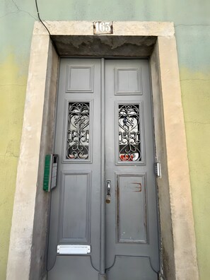 Une porte à deux battants, avec une plaque portant un numéro, un clavier et un interphone vert.
