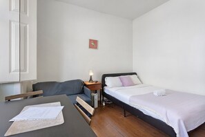 Une petite chambre à coucher, bien rangée, avec un lit simple, une table de chevet avec une lampe, une chaise et un bureau avec des papiers.