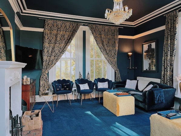 A room with a fireplace, a chandelier, a television, and a large window with curtains.