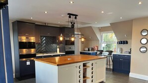 A modern kitchen with a central island, built-in appliances, and a herringbone-patterned backsplash. - Luxury Group Retreat | 20 Guests | Hot Tub + games room (Barnstaple)
