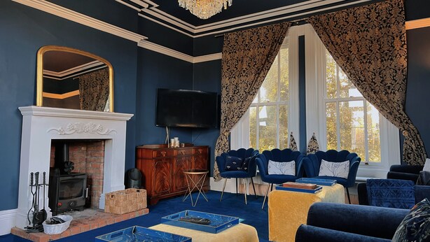 A room with a fireplace, a television, a chandelier, and a large window with curtains. - Luxury Group Retreat | 20 Guests | Hot Tub + games room (Barnstaple)