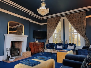 A room with a fireplace, a television, a chandelier, and a large window with curtains.