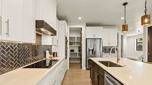 A modern kitchen with white cabinets, a herringbone backsplash, stainless steel appliances, and pendant lighting. - Horseman's Hideout 3 Bedroom Townhouse (Hurricane)