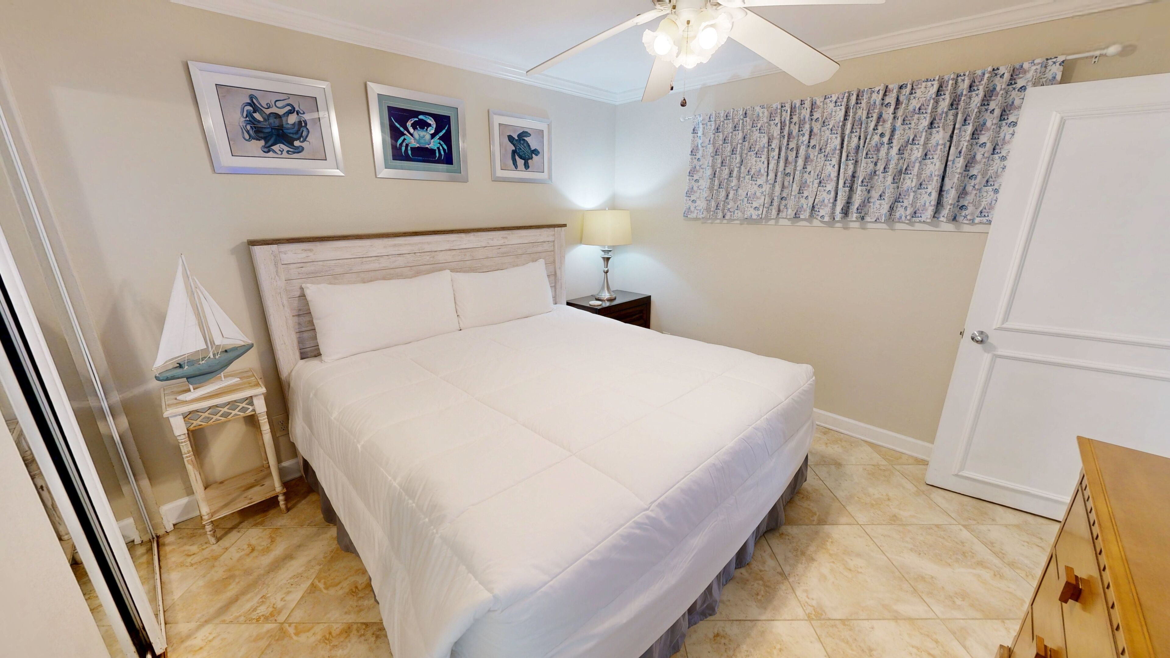 A bedroom with a bed, a nightstand, a lamp, a ceiling fan, and a door.