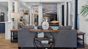 Een woonkamer met een grijze bank, een ronde salontafel en een boekenkast.