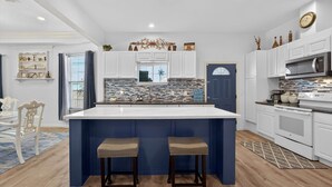 Een moderne keuken met een groot eiland, witte kasten en een blauwe accentmuur.