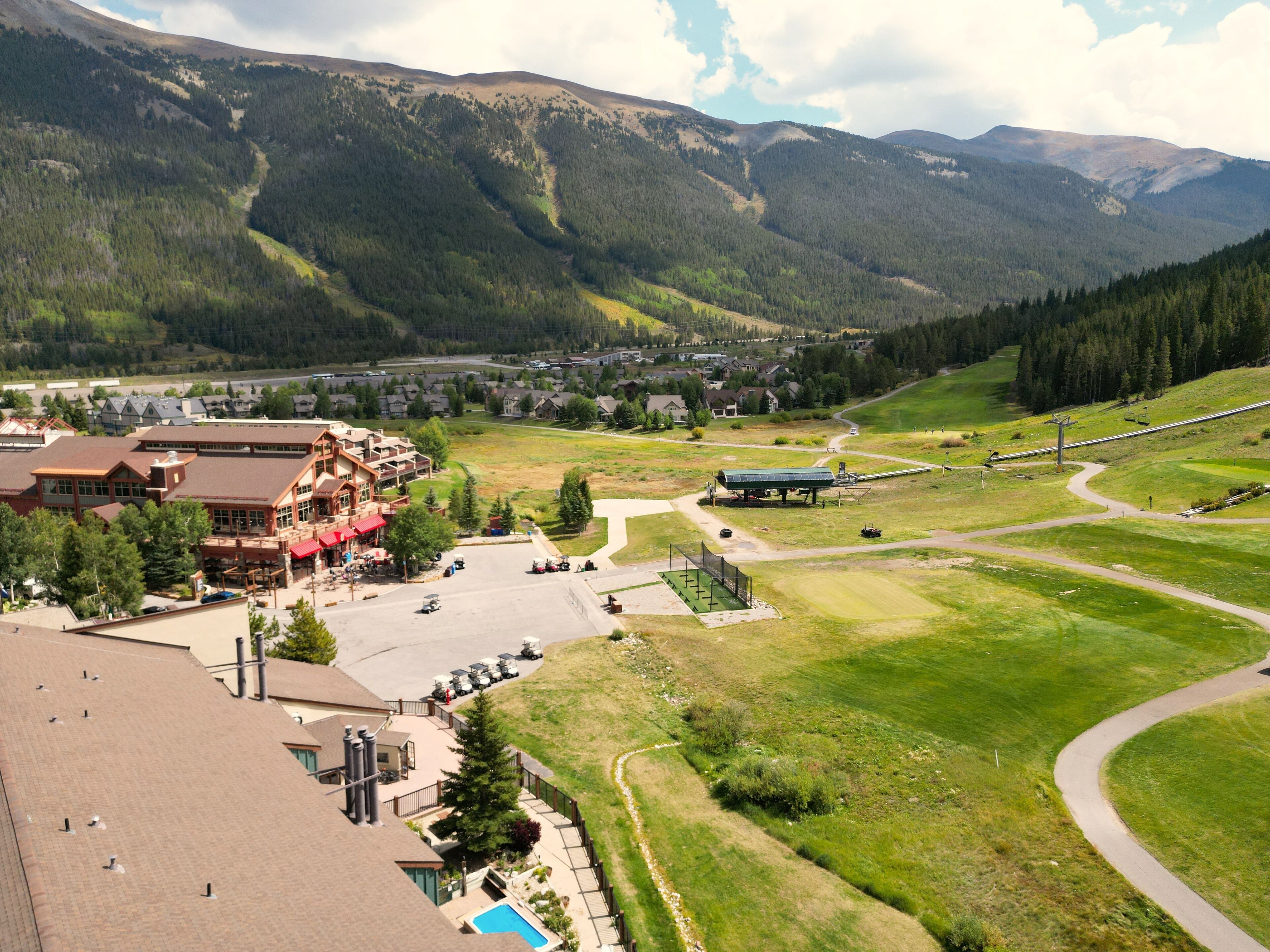 A mountain resort with a large building, a swimming pool, and a ski lift.