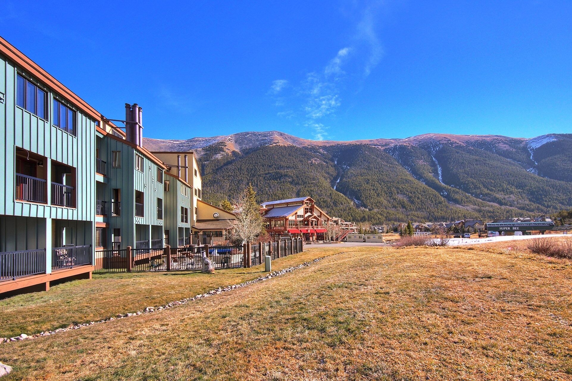 A hotel with a mountain backdrop, featuring a large building with multiple balconies and a visible outdoor seating area.
