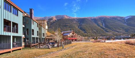 A hotel with a mountain backdrop, featuring a large building with multiple balconies and a visible outdoor seating area.